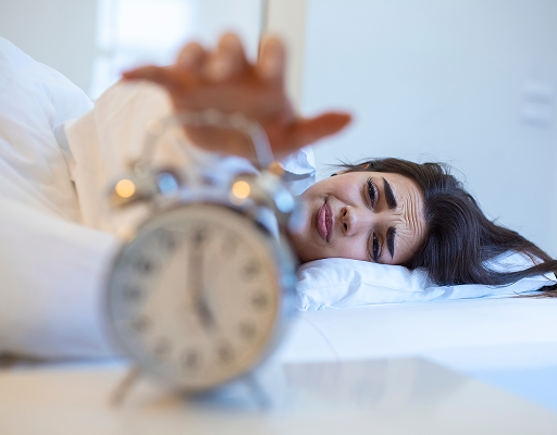 Woman waking up tired next to an alarm clock