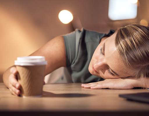 Tired woman resting her head on a desk beside a coffee cup